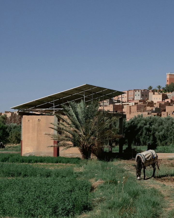 A small building with a solar panel roof in a green field